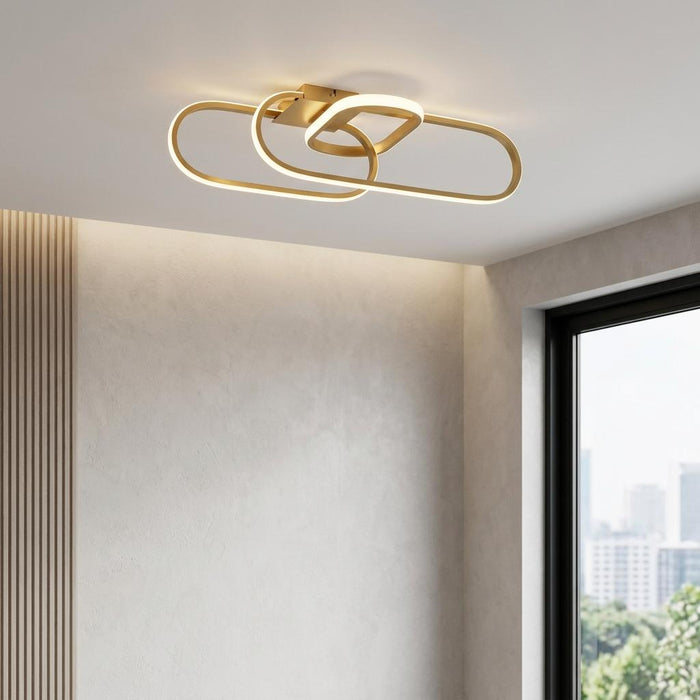 Modern gold LED flush ceiling light with interlaced oval loops mounted on a white ceiling.
