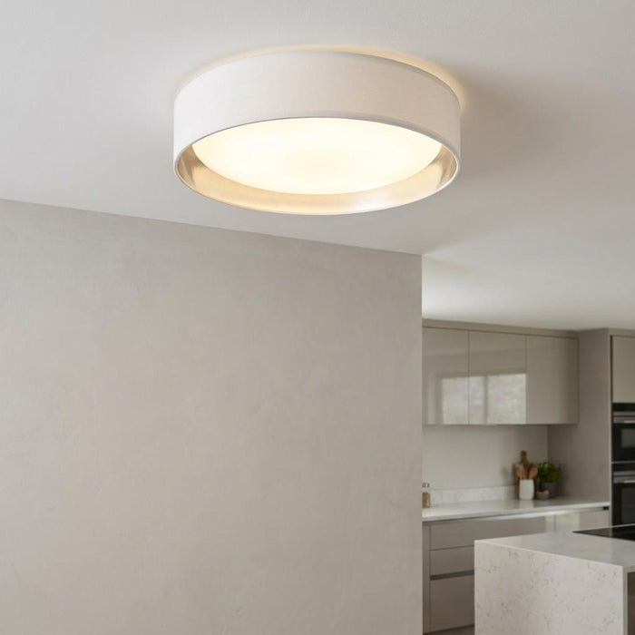 Modern flush ceiling light with a white fabric drum shade and silver interior lining, illuminated in a kitchen setting.