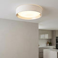 Modern flush ceiling light with a white fabric drum shade and silver interior lining, illuminated in a kitchen setting.
