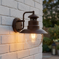 Rustic brown station-style outdoor wall light with a clear glass globe mounted on a white brick wall.