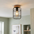 Industrial flush ceiling light with a black wire cage and wooden base, illuminating a sage green room.