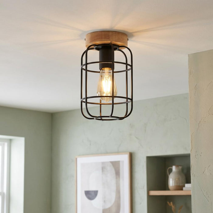 Industrial flush ceiling light with a black wire cage and wooden base, illuminating a sage green room.