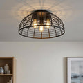 Matte black wire cage flush mount ceiling light with three glowing vintage-style bulbs.