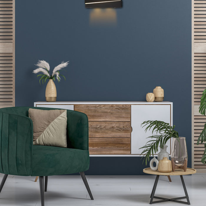 Section black wall light lit above a white sideboard in a navy living room with green armchair