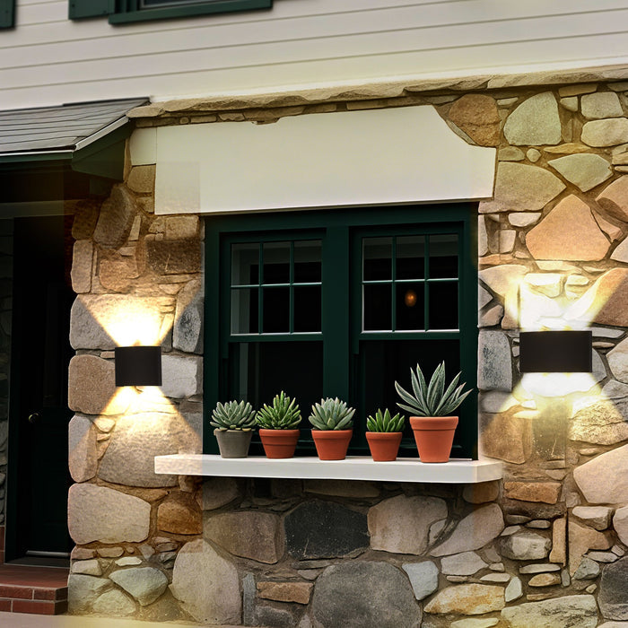 Shadows black wall lights up and down lighting a stone cottage window lined with potted succulents