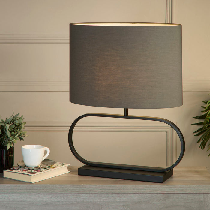Sleek black lamp with grey shade lit on a sideboard beside a teacup and foliage in a panelled room