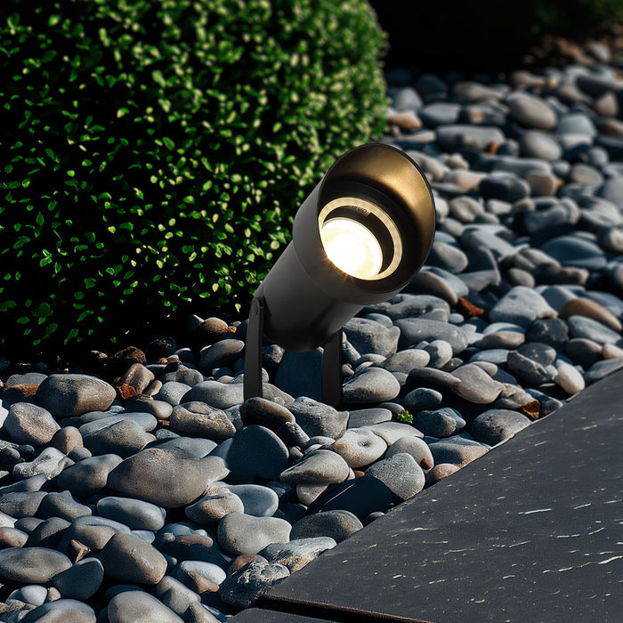 Spike black garden spotlight glowing among grey pebbles and uplighting a clipped shrub