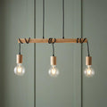 Three-light wooden linear pendant with wrapped black cords and glowing globe bulbs against a green paneled wall.