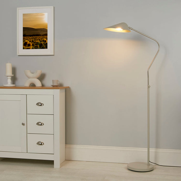 Swan curved-neck floor lamp lit in a grey room beside a cream sideboard, candle and framed print