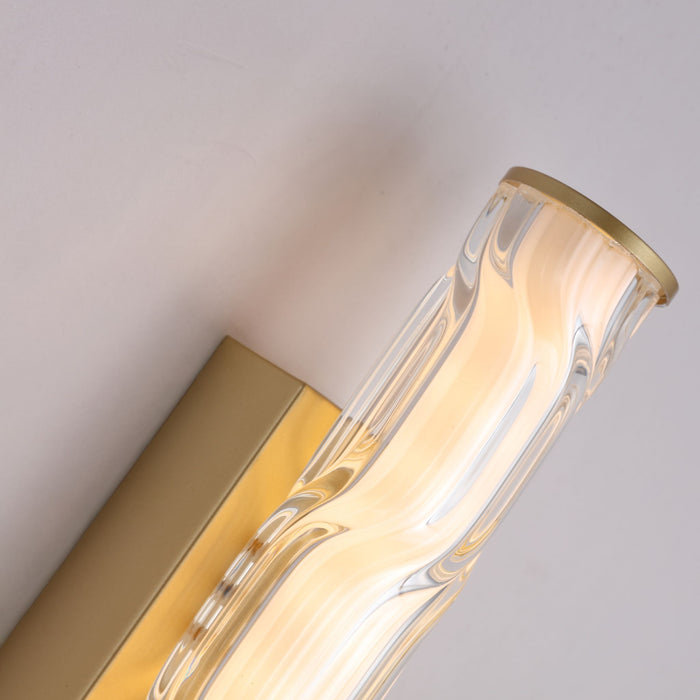 Close-up of the Vibrate wall light's brushed gold backplate and wavy clear glass tube end cap