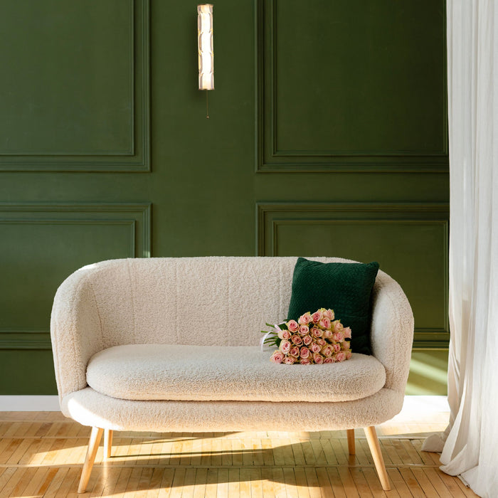 Vibrate gold wall light on a deep green panelled living room wall above a cream boucle sofa and roses